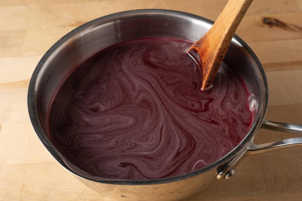 Stirring a pot of pomegranate grenadine with a wooden spoon.