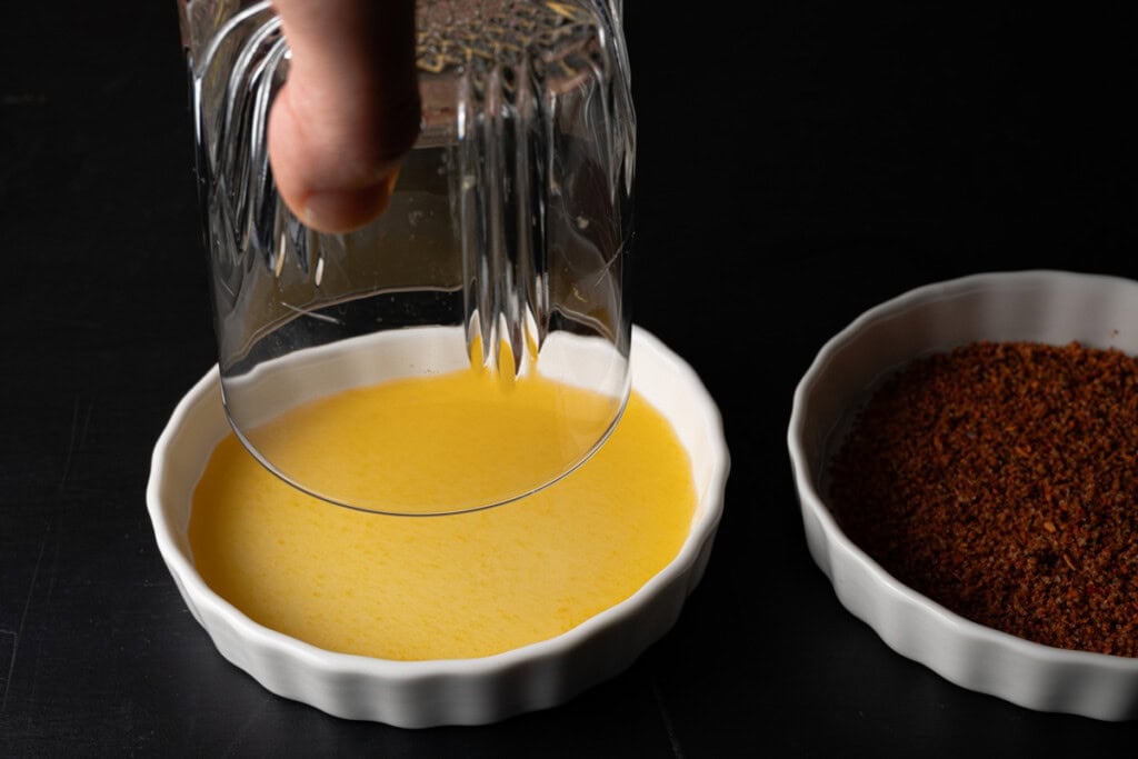 Dipping a cocktail glass rim into passion fruit syrup.