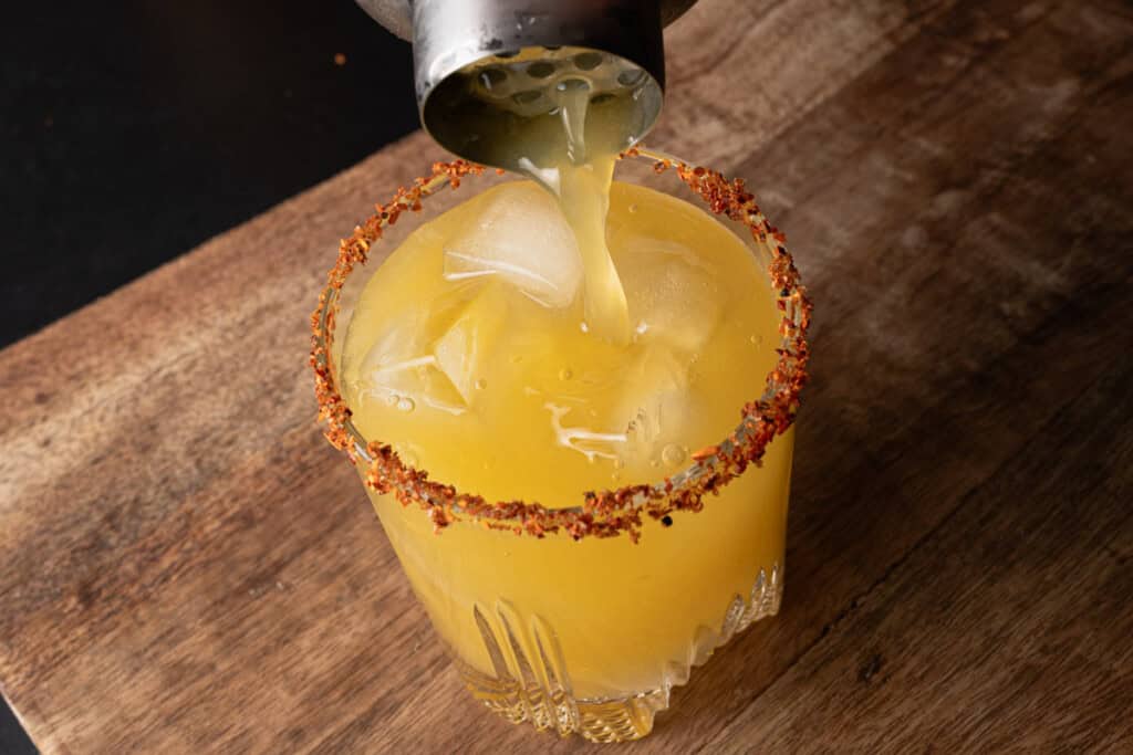 Pouring a passion fruit margarita over ice into a tajin rimmed glass.