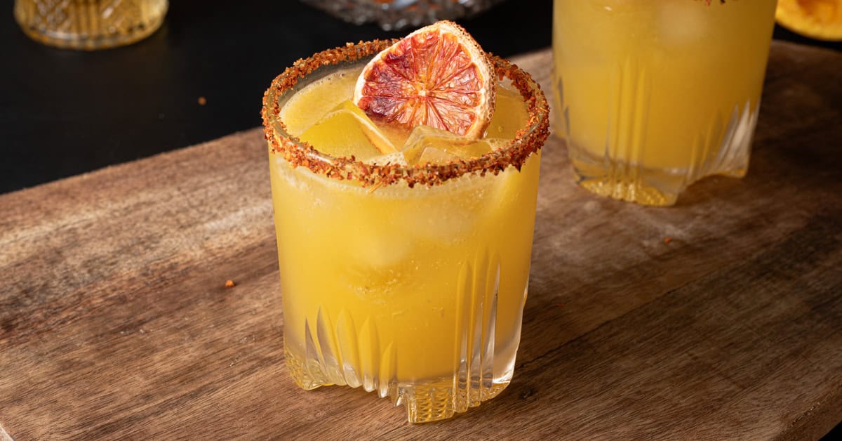 A passion fruit margarita on the rocks with a Tajin rim and a dried orange slice.