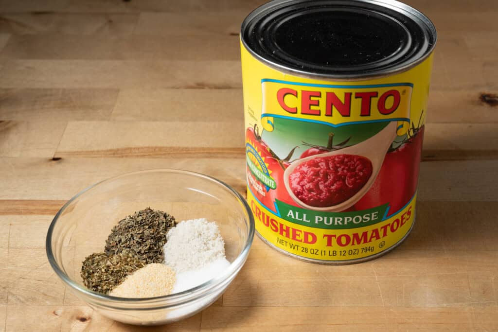 A can of crushed tomatoes and a bowl of spices for making homemade pizza sauce.